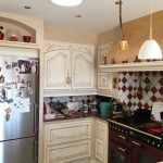 Cuisine sans fenêtre baignée de lumière naturelle par un conduit Solatube, avec meubles crème, cuisinière et crédence en carrelage rouge et blanc