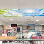 Intérieur de pharmacie avec panneaux de plafond MiraSky et présentoirs de produits. Panneaux « Promotions » et « Maquillage » visibles.