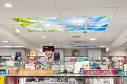 Intérieur de pharmacie avec panneaux de plafond MiraSky et présentoirs de produits. Panneaux « Promotions » et « Maquillage » visibles.