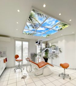 Cabinet dentaire moderne avec fauteuil et chaises oranges et plafond illuminé par des panneaux MiraSky.