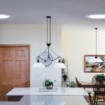 Cuisine lumineuse avec lumière naturelle provenant de tubes solaires au plafond et d'un éclairage suspendu au-dessus de l'îlot de cuisine.