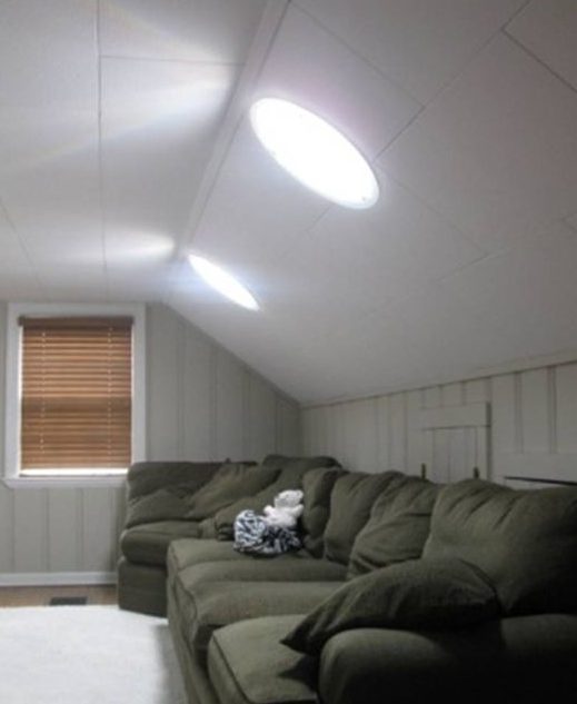 La lumière du soleil traverse les puits de lumière d'un grenier aménagé, illuminant un canapé sectionnel confortable.