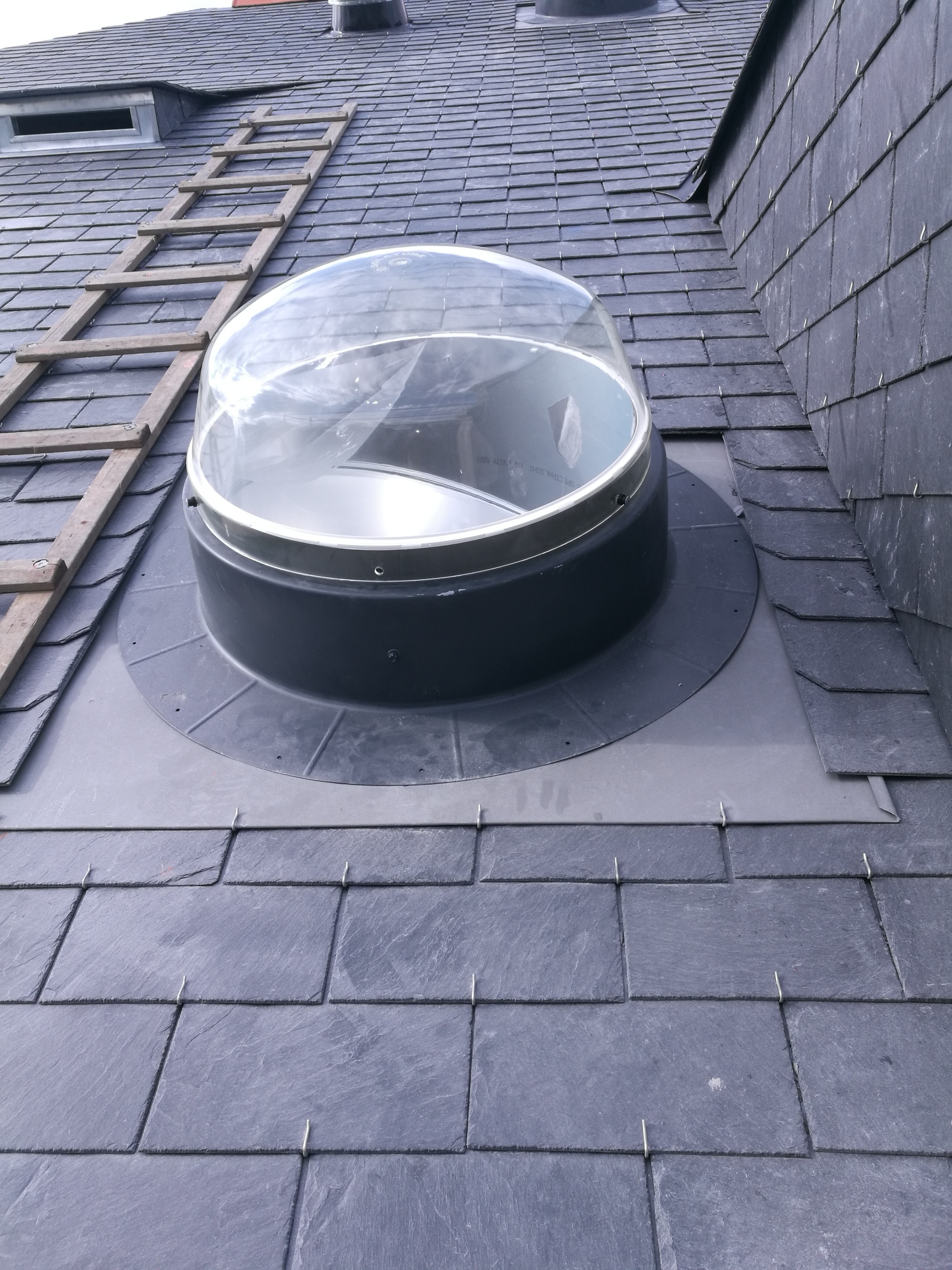 Conduit de lumière installé sur une toiture en ardoise.