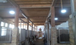 Intérieur d'une écurie avec des boxes en briques et des portes en métal.