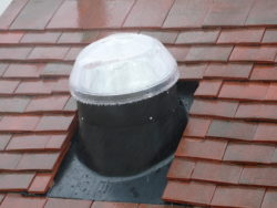 Conduit de lumière tubulaire sur un toit en tuiles rouges sous la pluie.